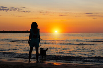 Backlit shadow of a woman with her dog on the beach during a sunrise with summer sky and copyspace