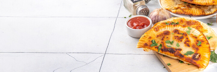 Chebureks, empanadas. Fried pies pasties, with meat and spices, on a white tiled background with herbs and tomato sauce 