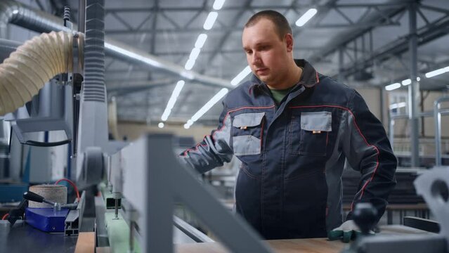 modern workshop in furniture factory, male controller works with automatic sawing machine