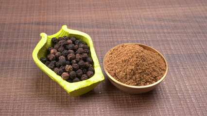 Black pepper in clay bowl on wood background with copy space. Healthy eating, ayurveda, naturopathy concept.