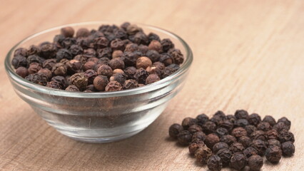 Black pepper in clay bowl on wood background with copy space. Healthy eating, ayurveda, naturopathy concept.