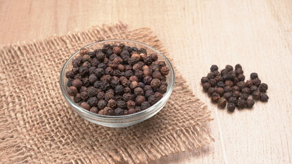 Black pepper in clay bowl on wood background with copy space. Healthy eating, ayurveda, naturopathy concept.