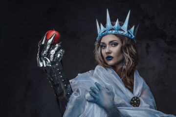 Portrait of attractive ice princess with red apple and frozen skin staring at camera.