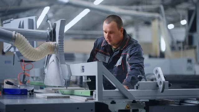 worker cutting wood and chipboard details by automatic sawing machine in modern workshop