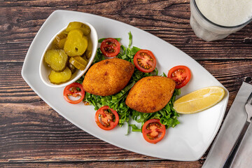 Kibbeh or icli kofte on a white porcelain plate with pickles and salad