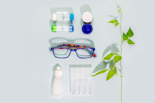 Oftalmology concept with kid eyeglasses, containers with contact lenses and moisturizing eye drops on blue background. Concept of eyecare, eye treatment and good vision. Flat lay