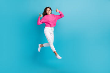 Full length photo of sweet confident lady wear pink pullover showing thumbs up jumping high empty space isolated blue color background