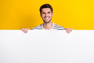 Photo of good mood pretty guy dressed striped t-shirt holding hands arms empty space isolated yellow color background