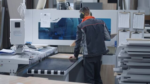 work in modern furniture plant, man is processing chipboard details by CNC router, automatic milling