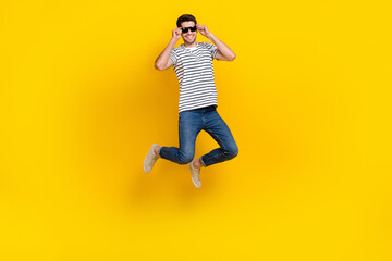 Fototapeta na wymiar Full length photo of funny cool guy dressed striped t-shirt dark eyewear jumping high having fun isolated yellow color background