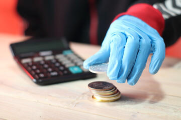 person in blue gloves holding a silver coin over a pile of coins against the backdrop of a calculator