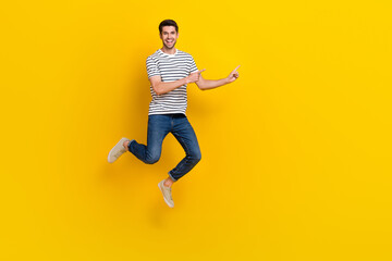 Obraz na płótnie Canvas Full length photo of cheerful cool guy dressed striped t-shirt pointing empty space jumping high isolated yellow color background