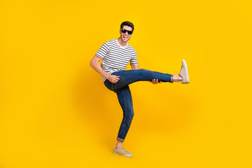 Fototapeta na wymiar Full length photo of excited cool man wear white t-shirt dark glasses playing leg guitar having fun isolated yellow color background