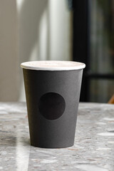 Morning coffee in black paper cup, take-away mug under light and shadown through tree.