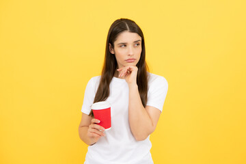 Beautiful woman in studio holding cup of coffee. Photo of cheerful positive pretty girlf holding mug of coffee smiling toothily isolated over yellow background.