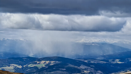 Rainclouds moving across the valley and the mountains of Seckauer Alps seen from Saualpe, Carinthia, Austria, Europe. Dark clouds accumulating and storm emerging. Thunder and rain over Central Alps