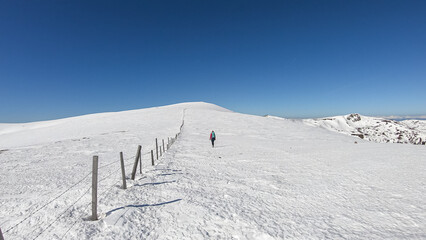 Woman hiking along fence on snow covered alpine meadow near Ladinger Spitz, Saualpe, Lavanttal...