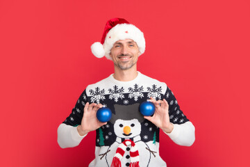 Man in holiday sweater and Santa hat on studio background. Santa with bauble, christmas ball.