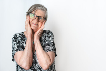 Cute old lady looking at camera with her hands holding her cheeks and sweet expression on white background