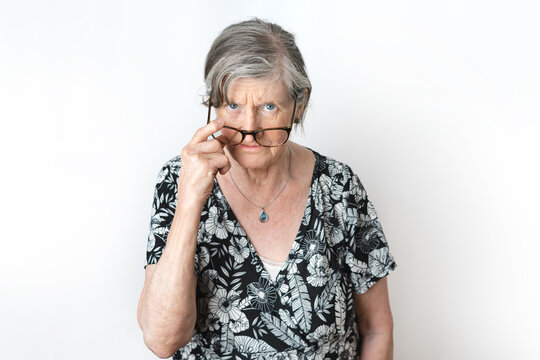 Portrait of angry senior woman peering over her eyeglasses on white background studio shot.