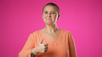 Smiling young gender fluid woman gives thumbs up 20s posing isolated on pink background studio. People sincere emotions lifestyle concept. Looking at camera with charming smile