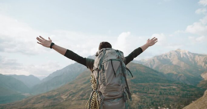 the camera moves around a man standing on the top of a mountain, raising his hands up and shouting from overflowing emotions of joy and a sense of satisfaction. The concept of achieving success