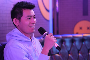 side view of one Asian young man holding microphone singing at karaoke - obrazy, fototapety, plakaty