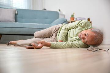 Sick senior old man falling down lying on floor because stumbled at home alone with wooden cane walking stick in living room, elderly man retired grandfather having accident after standing from sofa