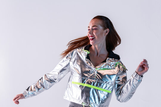 Cheerful woman in foil jacket dancing in studio