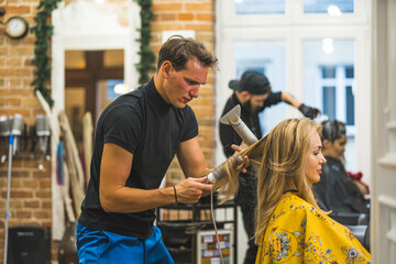 Professional male hairdresser drying and styling his female client's blonde hair with dryer in the professional hair salon . High quality photo