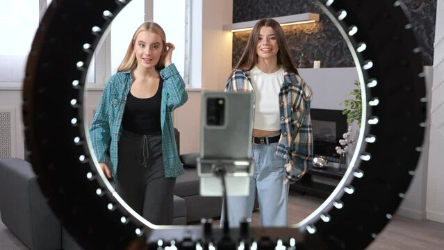 Two smiling girls creating content for social media. Teens dancing hip hop in front of a smartphone camera and ring light. High quality footage