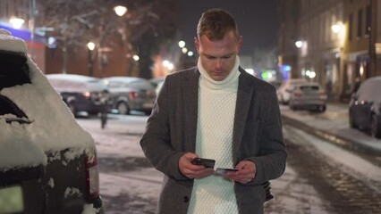 Man writing credit card number into mobile app for e-shopping standing outdoors under snowfall. Concept of electronic purchases on global network