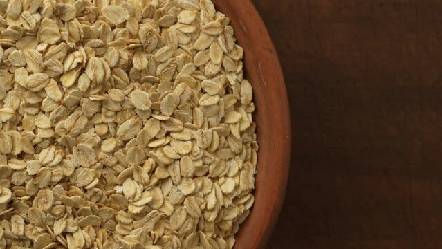 Dry oat flakes in a ceramic plate on a wooden background. Heap of oat flakes rotates, top view, close up, copy space for text