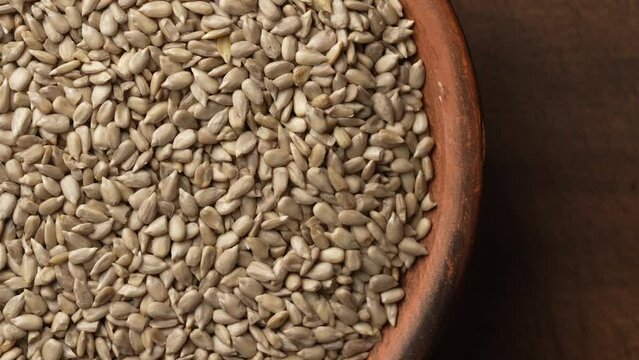 Grey raw sunflower seeds in ceramic bowl on a wooden background, rotate, close up, top view. Purified seeds of sunflower