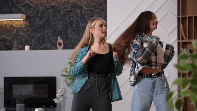 Two young beautiful female teens with long hair dancing hip hop at home or in the studio. Young bloggers move rhythmically to the beat of the music. High quality footage