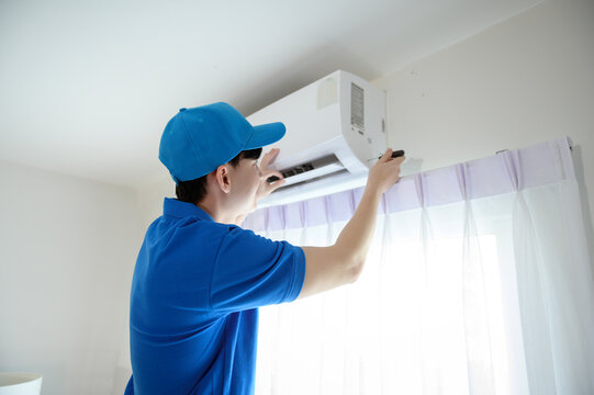 An Asian Young Technician Service Man Wearing Blue Uniform Checking ,  Cleaning Air Conditioner In Home