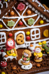 Christmas house made from gingerbread. Playfully decorated with colourful gummy bears. Christmas tree in background with lights. Festive New year atmosphere and mood. 