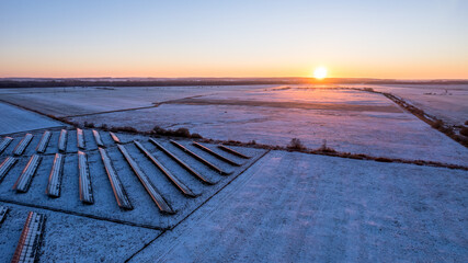 Aerial view of the solar farm during winter sunset. Blue sky, orange sun. Flight low over the white fields.  © Jakub Łukasik