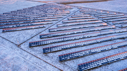Aerial view of the solar farm in a winter sunny day. Flight low over the white fields. Power...