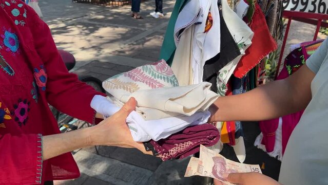 Closeup of hands exchanging Mexican Pesos money for traditional Mayan Mexican clothes from a street vendor in Merida, Yucatan, Mexico.