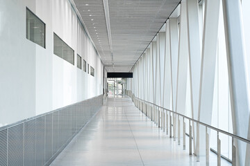 A corridor with white wall, glass facade and truss structure