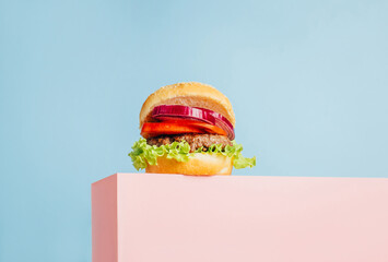 close-up on a hamburger on a pink cube on a blue background with free space for text