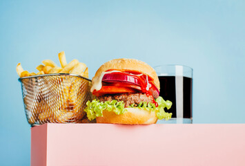 close-up on a hamburger and french fries and soda on a pink cube on a blue background with free space for text