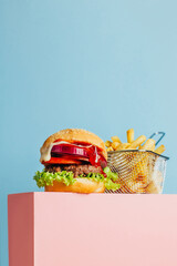 close-up on a hamburger and french fries on a pink cube on a blue background with free space for text