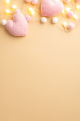 Fototapeta na wymiar Valentine's Day concept. Top view vertical photo of light bulb garland fluffy heart shaped toys and soft pompons on isolated pastel beige background with empty space