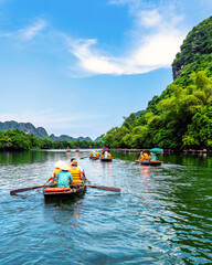 Tourists sitting on rowing boats enjoy the beautiful scenery of rivers and mountains in Trang An,...