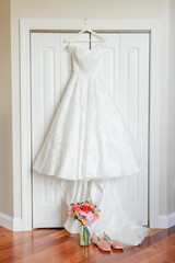 Wedding dress hanging with the brides bouquet and shoes