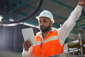 Professional Asian male engineer in helmet using the tablet to work, inspect and maintain electrical cabinet. Machines in a beverage factory, beverage industry concepts expert worker