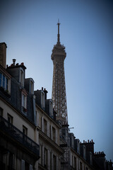 The top of the Eiffel Tower towering above the roofs of Parisian buildings