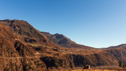 A wilderness of rocky desert with barren brown mountains of great Indian Himalayas amid clear blue sky with a narrow road to distant villages.